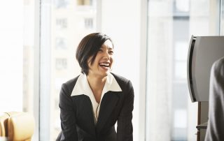 Businesswoman at desk smiiling at businessman