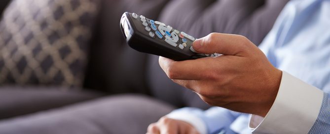 Close Up Of Man Sitting On Sofa Holding TV Remote