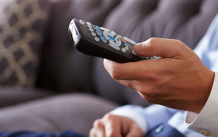 Close Up Of Man Sitting On Sofa Holding TV Remote